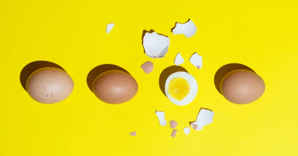 Huevo cocido pelado y huevos frescos sobre fondo amarillo

