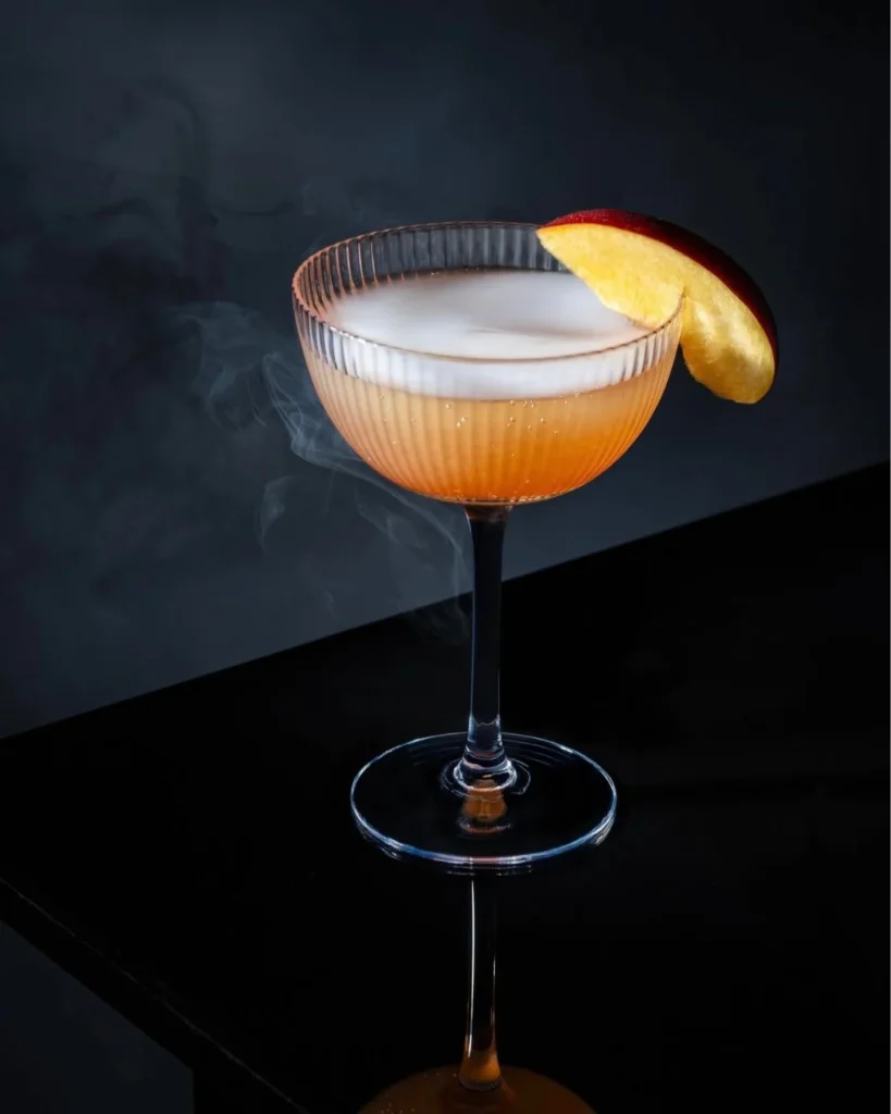Cóctel Bellini con puré de durazno en copa de cristal estriado, fotografía artística de coctelería veneciana.