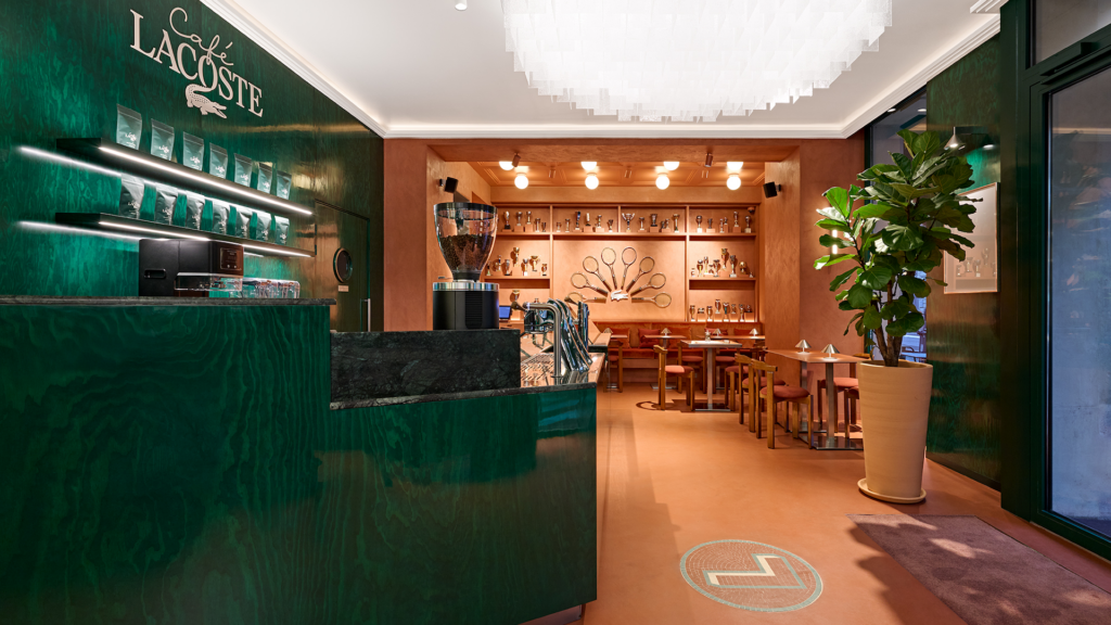 Diseño interior del Café Lacoste en París con paleta de colores verde profundo y acentos en terracota, fusionando arquitectura contemporánea con el ADN deportivo de la marca.