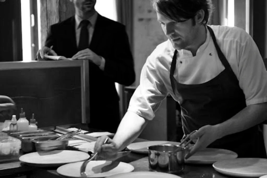 El chef René Redzepi trabajando en la cocina de Noma, concentrado durante el proceso de emplatado final de una creación culinaria que ejemplifica su enfoque en el detalle y la precisión técnica.