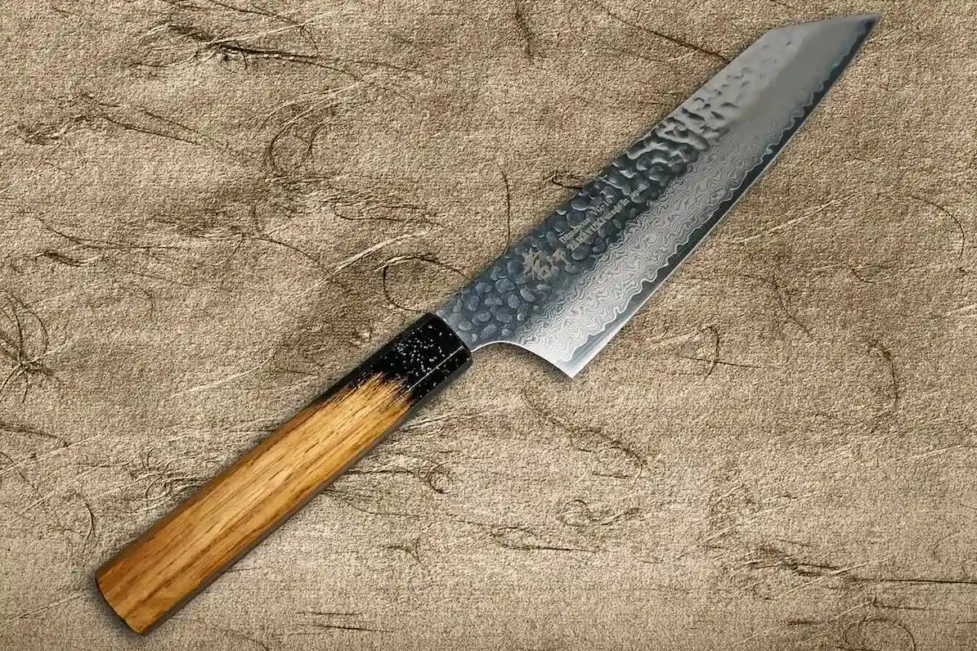 Detalle de la hoja de acero Damasco de 33 capas del cuchillo Gyuto de Sakai Takayuki, mostrando el patrón característico de pliegues sobre un fondo neutro.