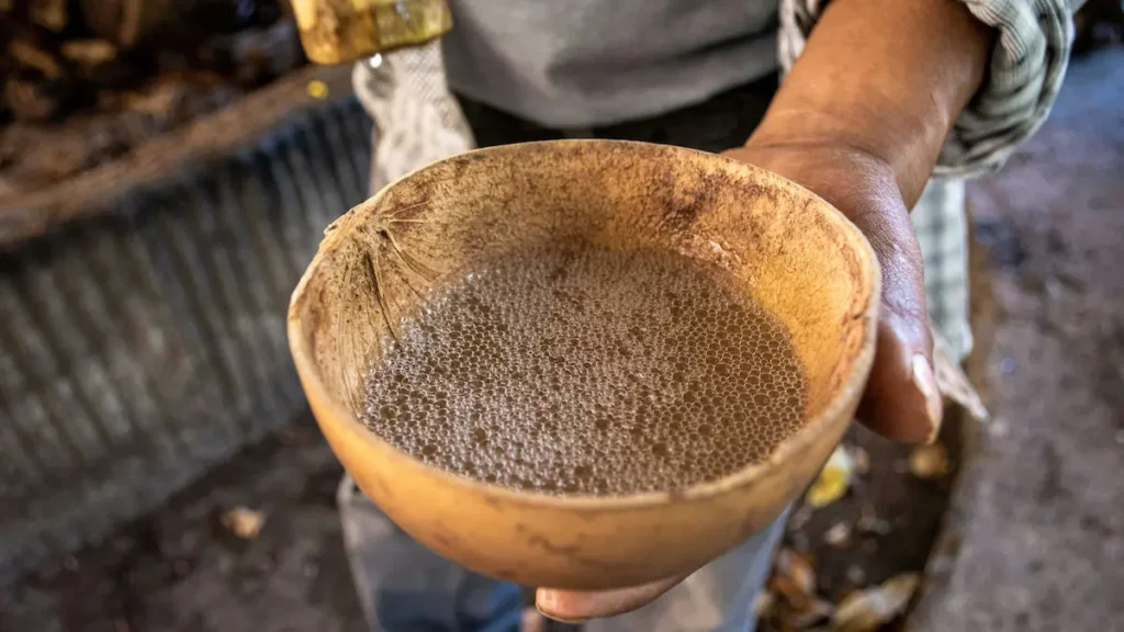 Mano sosteniendo una jícara con mezcal destilado dentro.