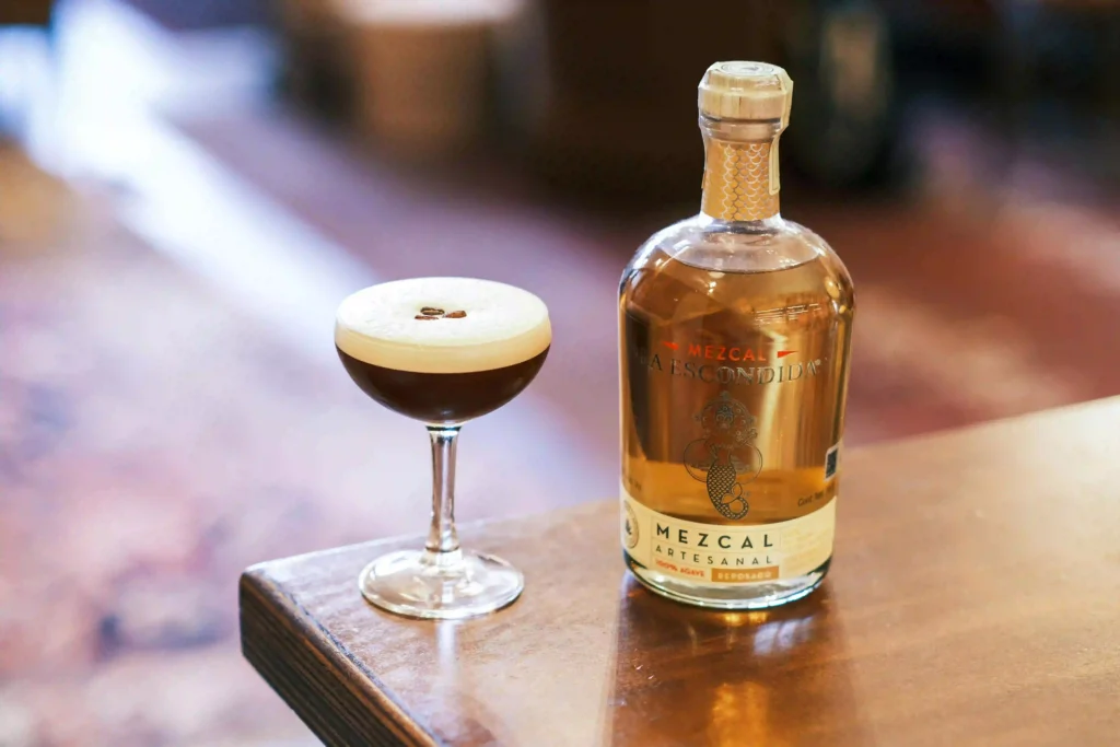 Botella de mezcal sobre mesa, junto a un cóctel creado con ese destilado.