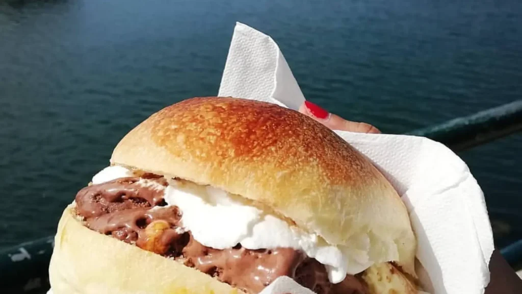Tradicional brioche con gelato del Bar Nettuno en Salerno: un pan dulce tipo brioche relleno de generosas bolas de helado artesanal y nata montada, servido frente al mar.