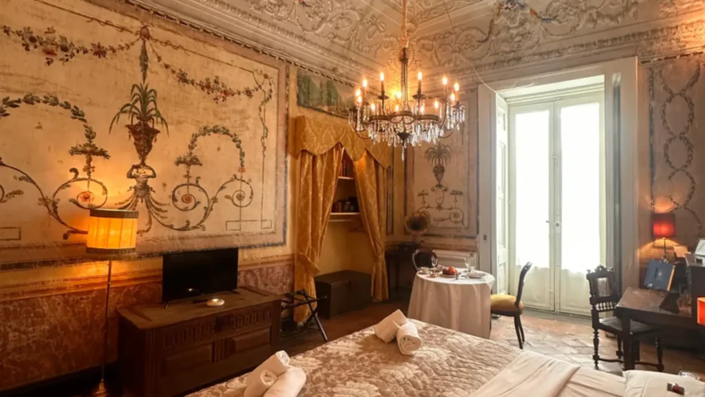 Interior de la suite de lujo en Palazzo Santangelo, Salerno; destacando techos altos con frescos originales, mobiliario de época y un majestuoso candelabro de cristal suspendido.