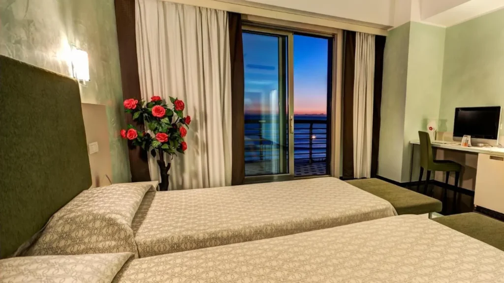 Habitación del Grand Hotel Salerno con vistas directas al mar durante el atardecer, capturando los tonos anaranjados del cielo sobre el puerto y el horizonte del Tirreno.