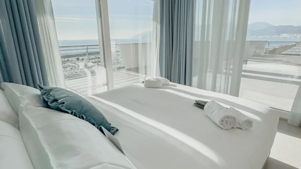 Suite de lujo en Lilibeth Luxury Suites, Salerno; con ventanales de cristal de piso a techo que ofrecen una vista panorámica inundando la habitación de luz natural y diseño minimalista.