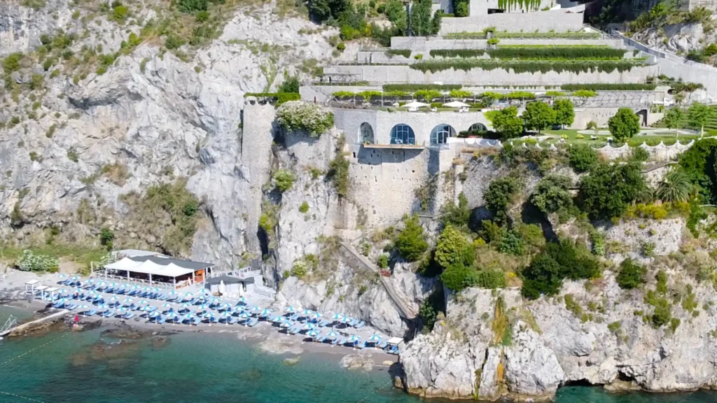 Vista panorámica del Riva Beach Club en Salerno, con filas de sombrillas blancas organizadas simétricamente frente al mar cristalino y la costa de la Campania al fondo.