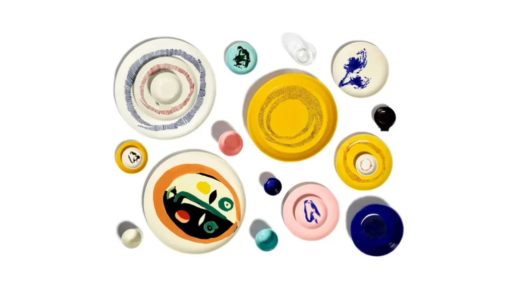 Toma cenital de la vajilla de diseño de Yotam Ottolenghi. Platos de colores vibrantes en tonos azul, amarillo y rosa dispuestos sobre una mesa, decorados con una variedad de platillos coloridos.