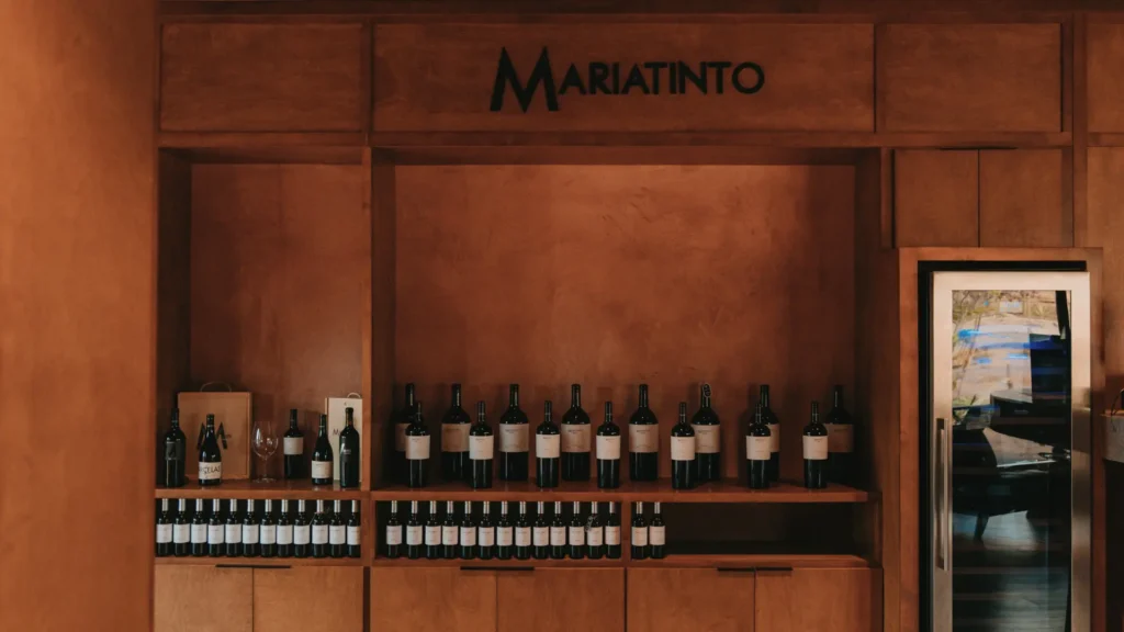 Estantería de madera con botellas de vino y logotipo de Mariatinto en su nuevo espacio en Valle de Guadalupe, Baja California.
