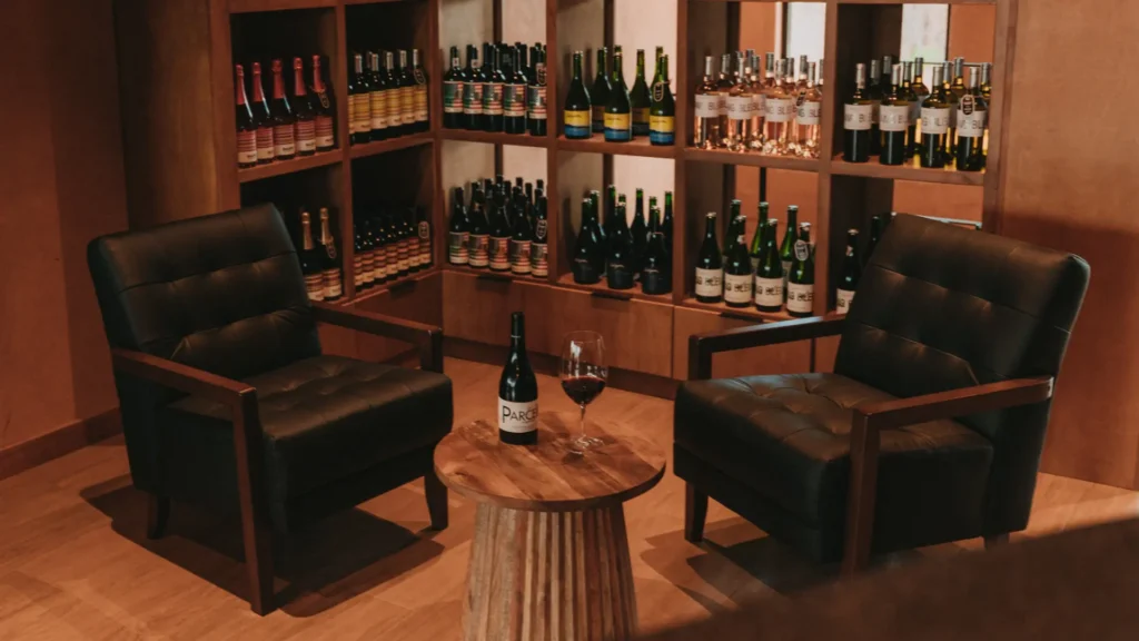 Dos sillones negros y una mesa de madera con una botella y copa de vino en Espacio Mariatinto, Valle de Guadalupe.