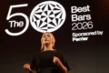 Presentadora vestida de negro frente al logotipo oficial de The World's 50 Best Bars 2026 durante la ceremonia de premiación.