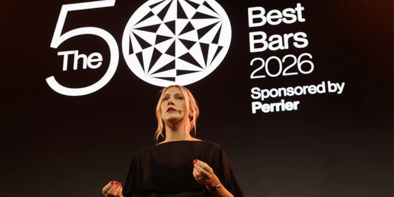 Presentadora vestida de negro frente al logotipo oficial de The World's 50 Best Bars 2026 durante la ceremonia de premiación.